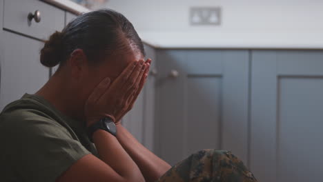 depressed female soldier in uniform suffering with ptsd sitting on kitchen floor on home leave