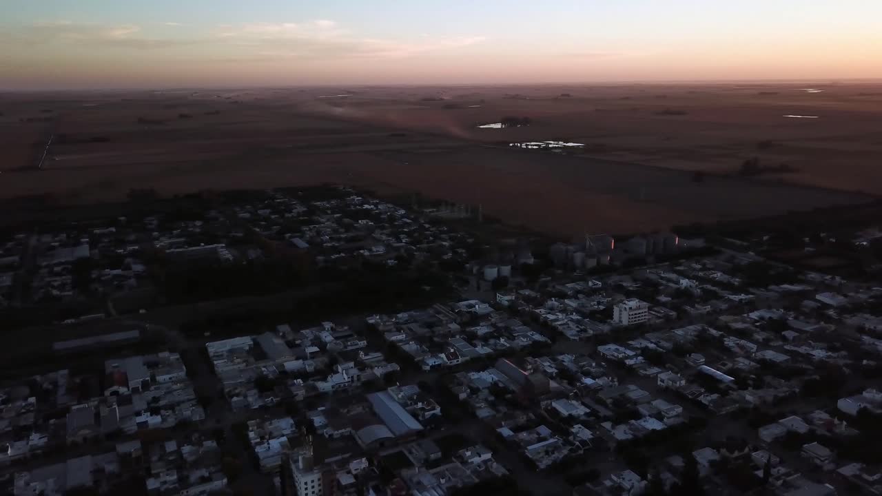 Drone Aerial panning view of a country city in the sunset with trucks dusty clouds in the horizon in the harvest time