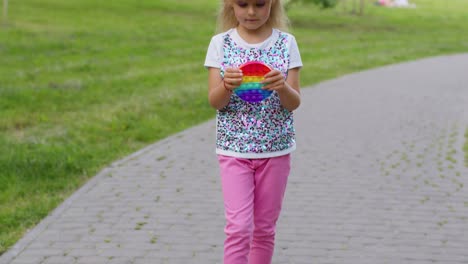 Child-girl-kid-playing-push-pop-it-bubble-fidget-toy-in-park,-stress-anxiety-relief-squeeze-sensory