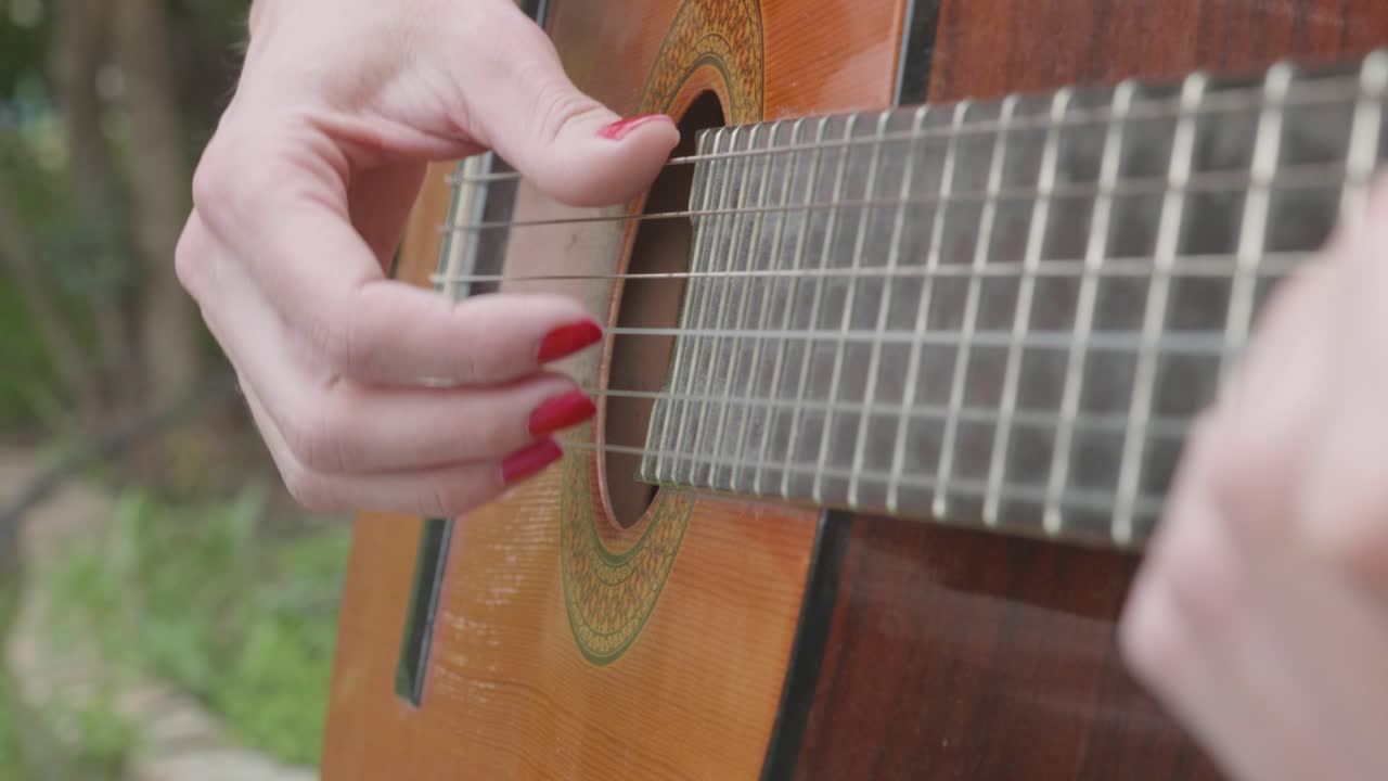 woman with red painted nails plays a spanish guitar