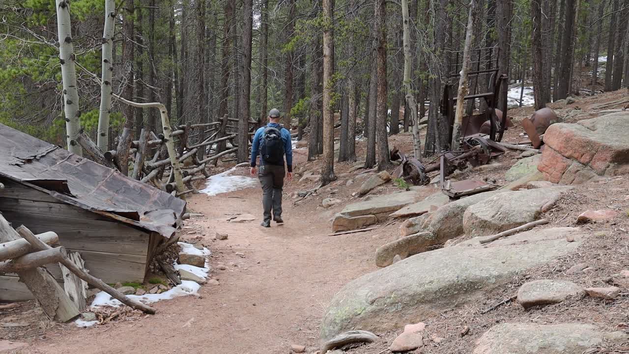 A man walks by a remote abandoned cabin along a trail in pine forest. Filmed in Staunton State Park during the spring.