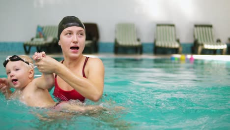 slow motion shot of happy smiling little kid swimming together with his mother in the swimming pool. young mother is turning him