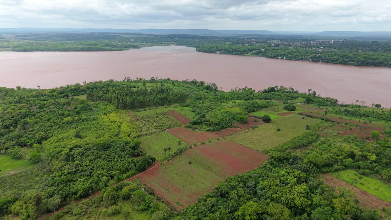 High-altitude drone reveals patches of agricultural fields, plantations, and green forest in Campichuelo, with Paraná river near by