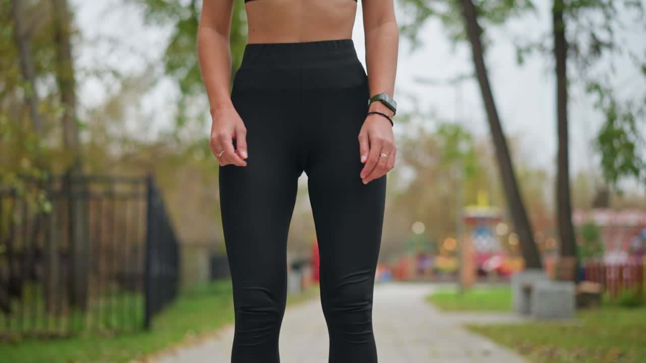 Young athlete performing squat exercise outdoors in game park with blurred background showcasing trees and colorful game machines,focus on fitness and strength training