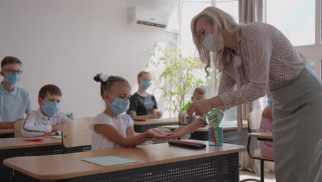 The-teacher-treats-the-hands-of-an-antiseptic-girl-in-the-classroom-at-school-before-class.-coronavirus-and-the-pandemic-at-school.-The-work-of-the-school-in-the-epidemic-mode