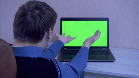 un tipo con una máscara protectora está emocionalmente enojado por una conexión remota en una videoconferencia y golpea sus puños en una computadora portátil, pantalla verde