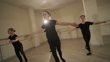 a group of young ballet students in black dancewear practicing positions in a spacious ballet studio with wooden flooring and wall-mounted barres. focused expressions and synchronized movements.