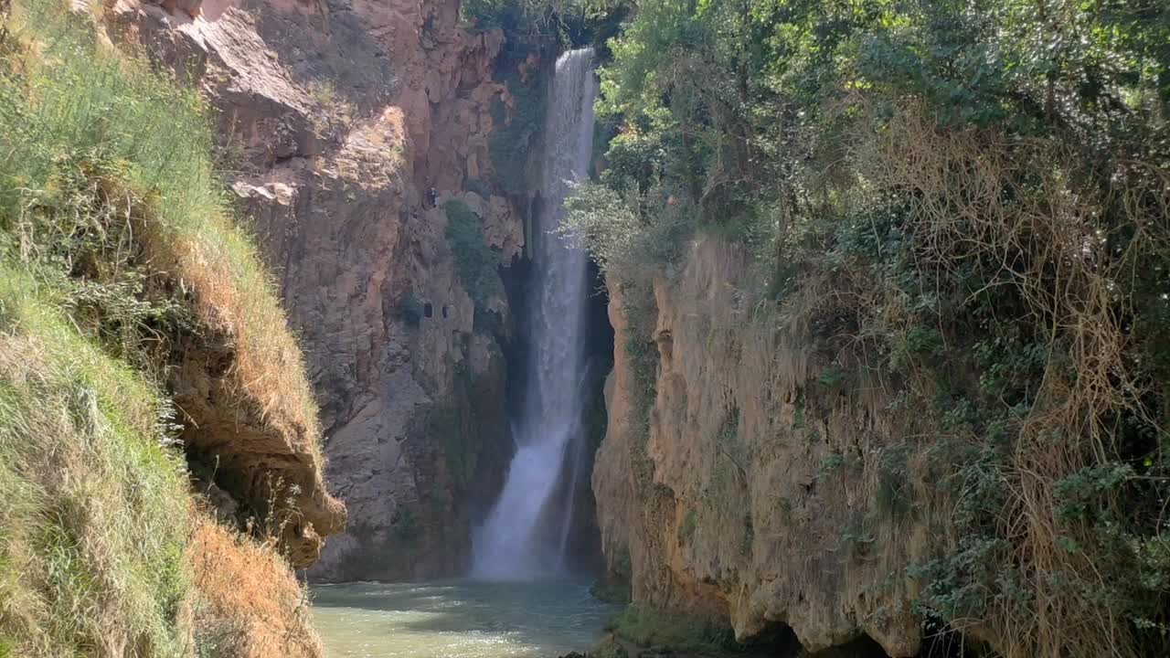 Static shot of tall waterfall surrounded by rocky cliffs and vegetation at Monasterio de Piedra