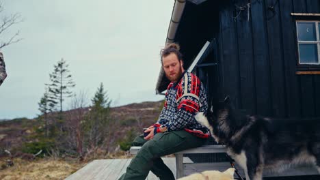 norwegian guy with alaskan malamute dogs resting outside the mountain lodge. static shot