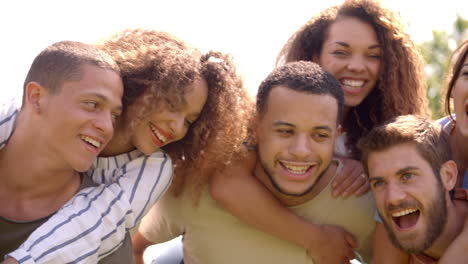 Close-up-of-six-young-adult-friends-piggybacking-outdoors