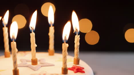 close up de velas encendidas en un blanco, pastel de cumpleaños decorado, luces bokeh en el fondo