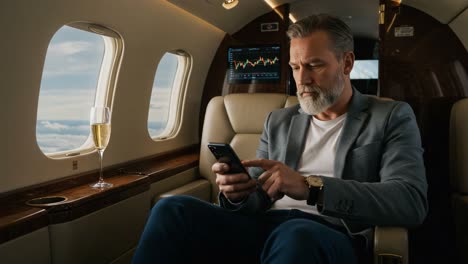 sophisticated businessman relaxing in a private jet, engaged with a smartphone, enjoying champagne while enjoying scenic aerial views.
