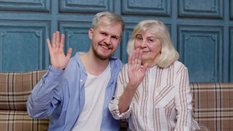 family of senior gray-haired mother and handsome adult son or grandson waving hi, hello, welcome