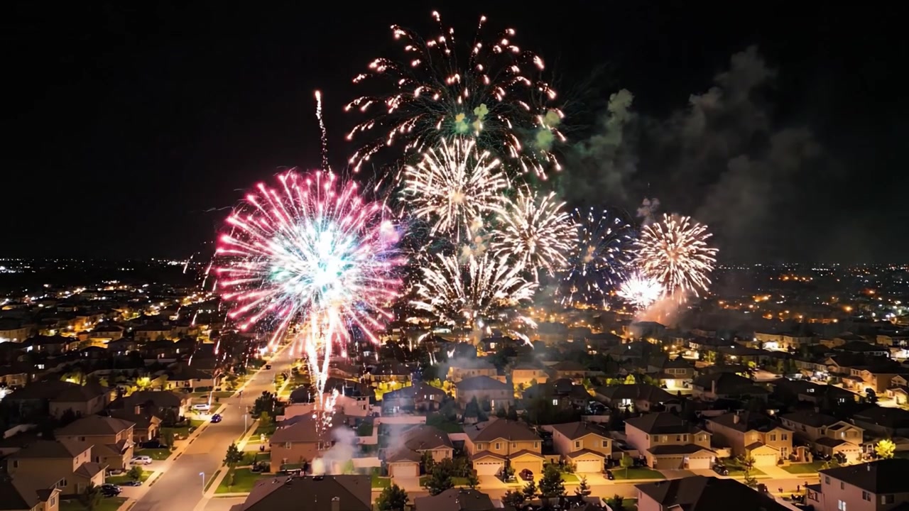 Uno spettacolo pirotecnico abbagliante illumina un quartiere residenziale, creando un'atmosfera di festa sotto il cielo notturno, pieno di esplosioni e luci colorate