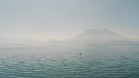 drone aerial flying towards a man on a boat during the morning in lake atitlan, guatemala