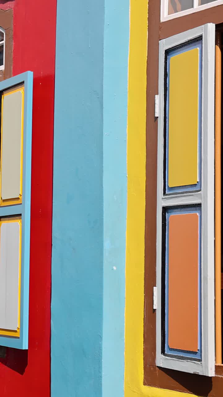 A câmera desliza suavemente por uma fachada vibrante e multicolorida de um edifício histórico com uma janela de madeira aberta, sob a luz natural brilhante do dia em Singapura.