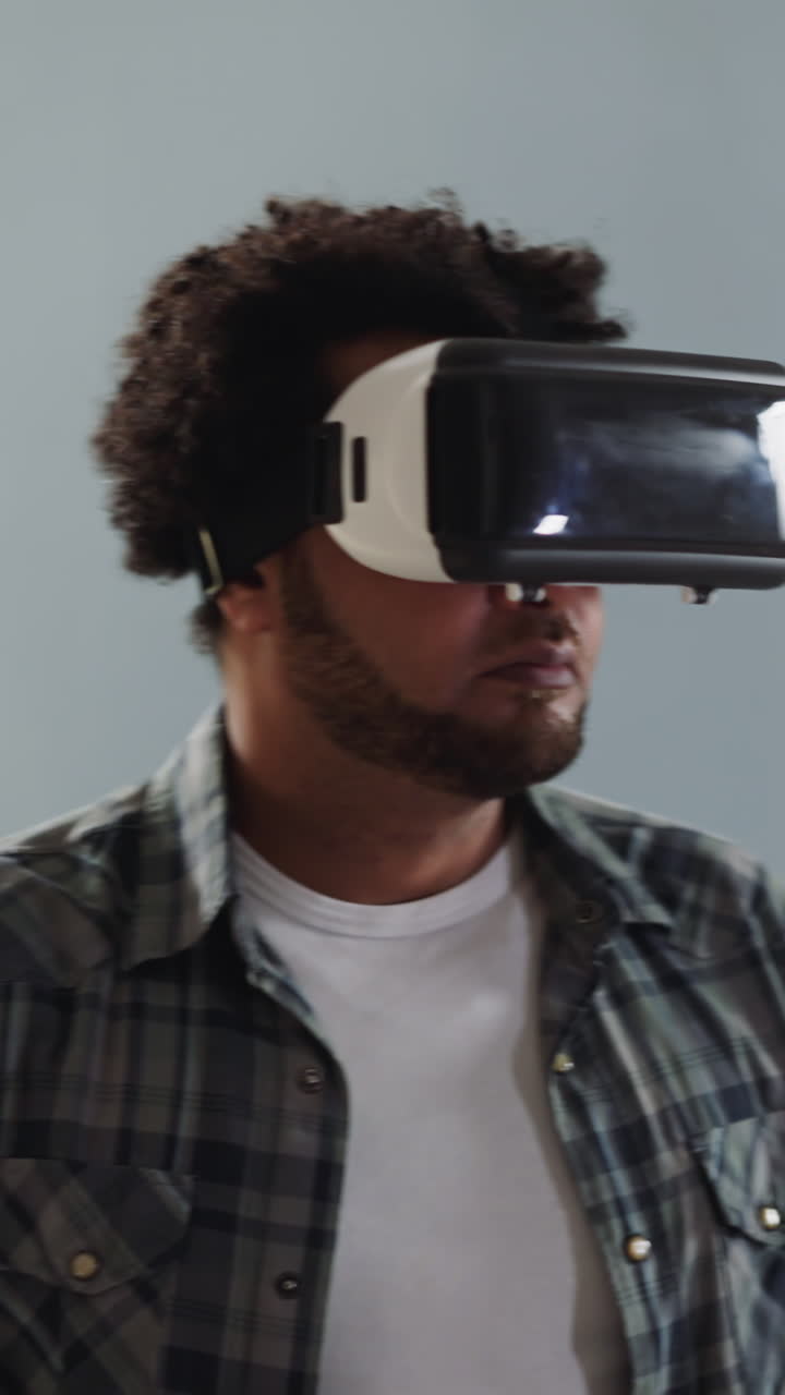 Black bearded guy with VR helmet turns around on grey background close view. Cyberspace technology for life experience. Business and amusing device