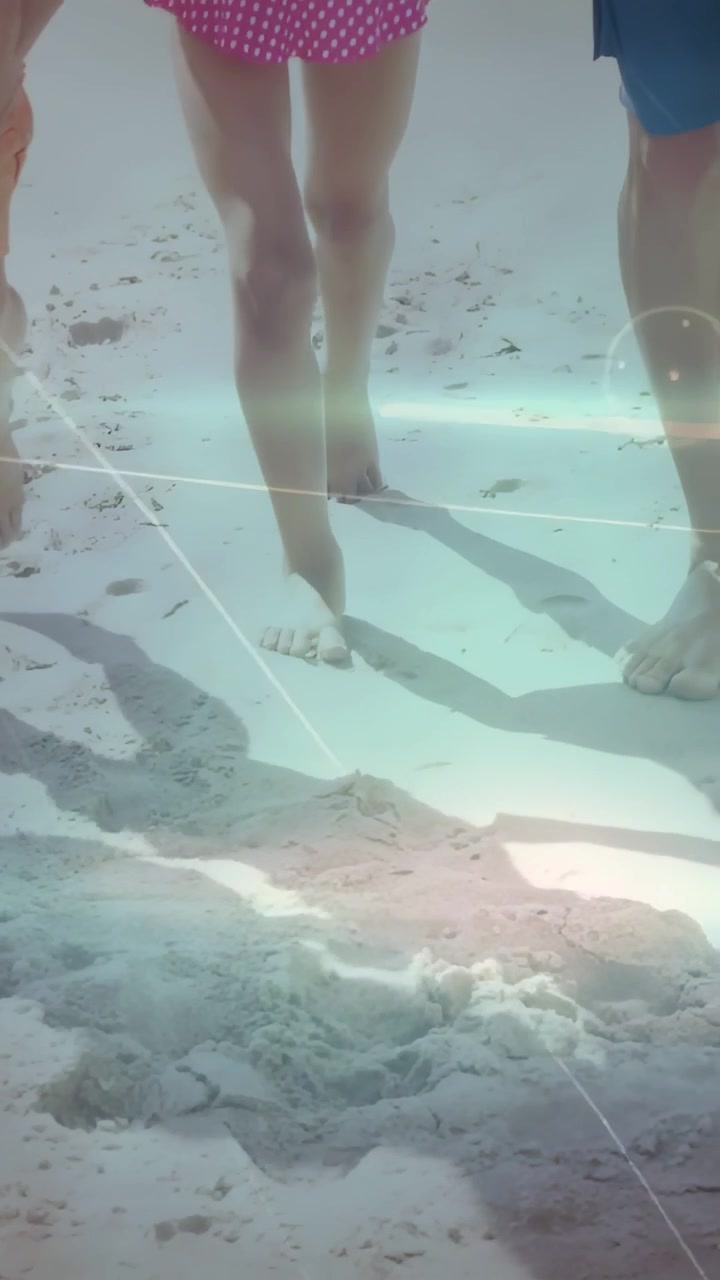 Vertical video: Sunlight starting close-up, family legs walking, leaving footprints toward surf