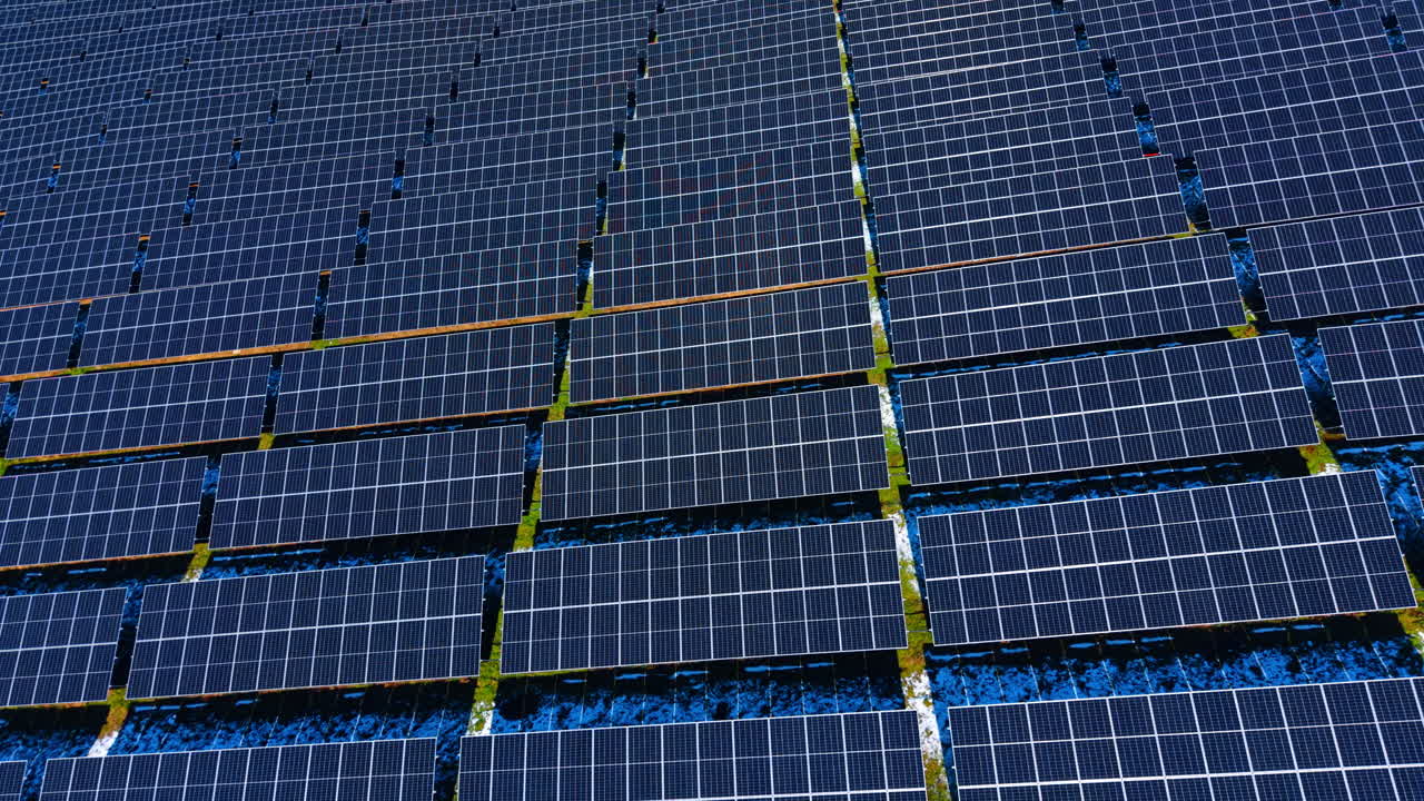 Vista dall'alto simmetrica di pannelli solari su terreno erboso. Motivo geometrico dall'alto di moduli fotovoltaici con superfici blu e bordi di erba verde.