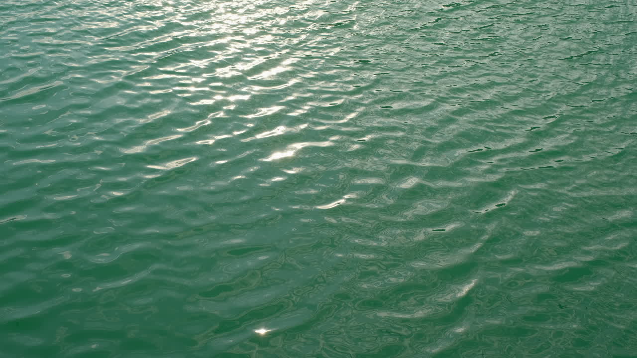 Surface of water with small ripples Light reflects off the waves creating bright spots Close up view of the water's texture