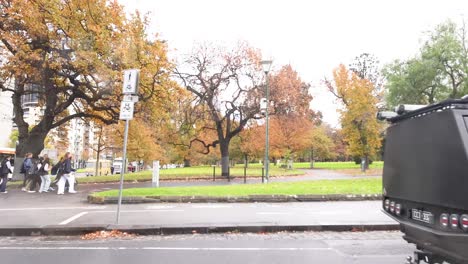 vehicle passing by park with pedestrians