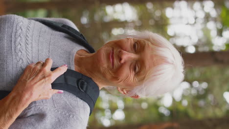 active retired senior woman walking in woodland countryside wearing backpack breathing fresh air