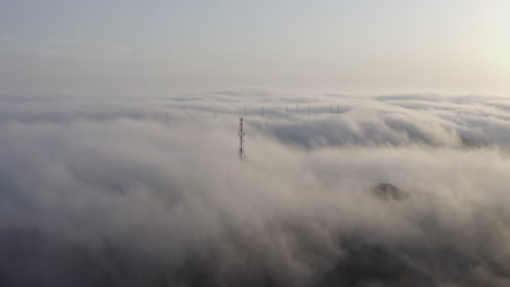 array of telecommunication towers sticking out of a dense heavy fog, moving over hills in the afternoon