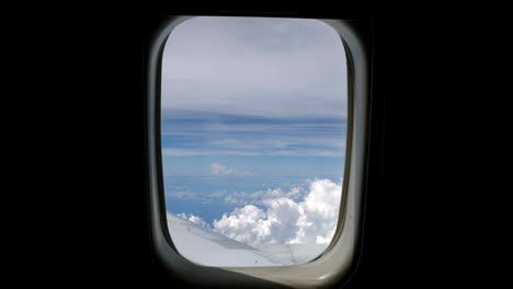 static shot of airplane window with white clouds and blue sky in background