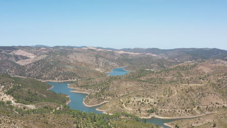 drone flight over a reservoir that occupies an entire valley between the mountains in a clear blue sky