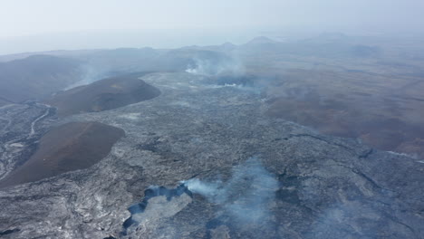 Jenseitiger-Luftdrohnenblick-Auf-Die-Rauchige-Lavalandschaft-Des-Vulkansees,-Die-Rückwärts-Fliegende-Drohne-Zeigt-Den-Fagradalsfjall-Kraterkegel,-Island,-Sonnigen-Tag