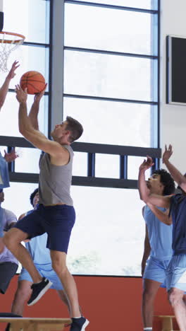 vertical video of diverse male basketball team training in indoor court, in slow motion