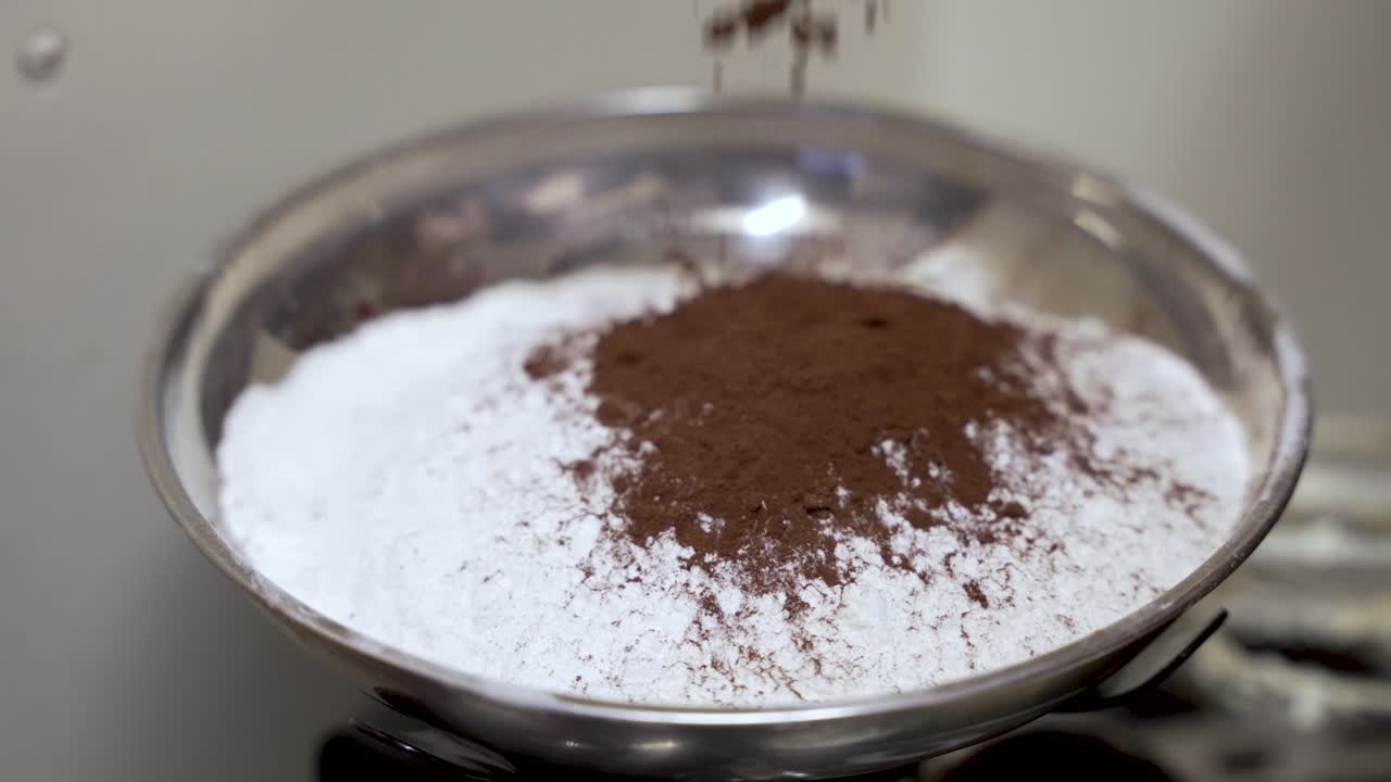 Cocoa powder being poured into a bowl of white flour, showing baking preparation. slow motion
