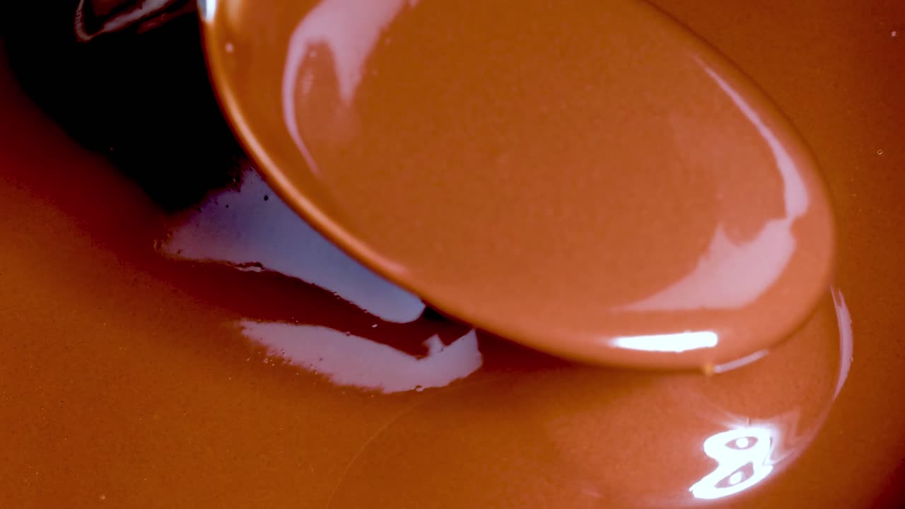 Un cucchiaio mescola delicatamente e solleva cioccolato liscio e lucido, mettendone in risalto la ricca consistenza e la lucentezza.
