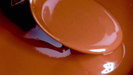 a spoon gently stirs and lifts smooth, glossy chocolate, showcasing its rich texture and shine.