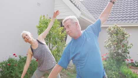 Relaxed-caucasian-senior-couple-practicing-yoga-in-front-of-house