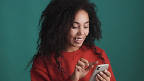 african american smiling woman using smartphone over blue background.