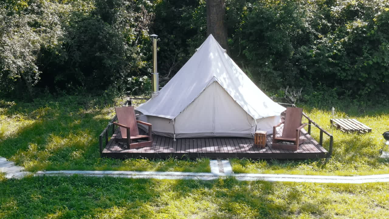 Glamping tent with chairs in the nature, green grass and trees, trail