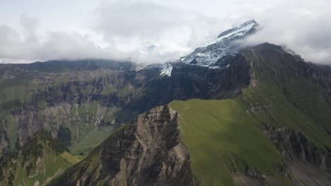 Descending-aerial-shot-over-Morgenberghorn-in-Switzerland-moving-forwards-to-the-edge-of-the-mountain-ridge-and-its-rocky-and-grass-side-in-contrast-to-each-other