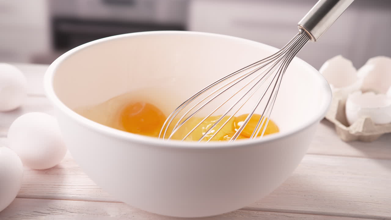 batir huevos para el desayuno en un tazón blanco con batedor de huevos en una mesa de la cocina, cámara lenta