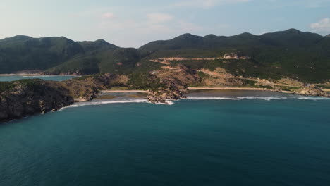 Beautifully-clear-blue-sea-that-gently-ends-on-the-beautiful-sandy-beaches-of-Vinh-Hy-Bay-in-Vietnam-with-the-high-green-mountains-in-the-background