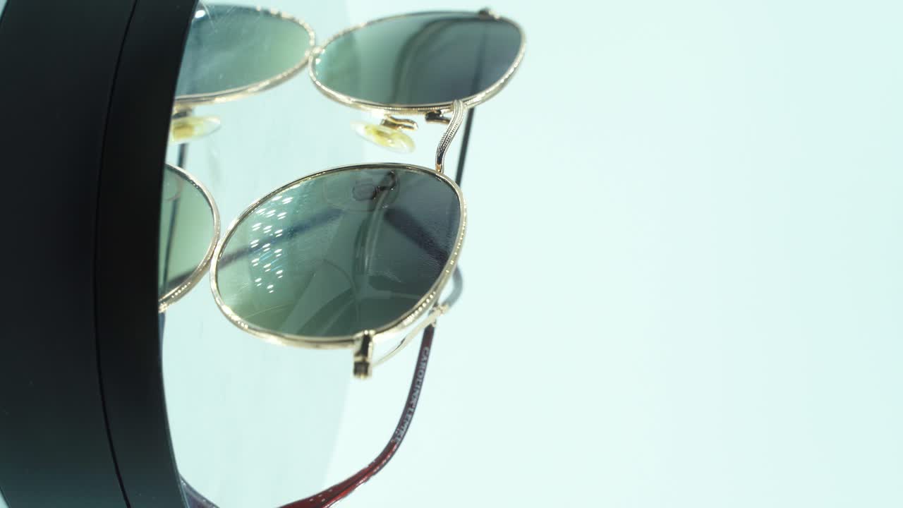 360도 회전 스탠드에 금색 선글라스를 놓는 수직 근접 촬영, 그을린 유리, 스튜디오 조명, 제품 4k 비디오, 느린 동작