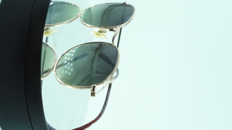 una toma cinematográfica vertical de colocar gafas de sol doradas en un soporte giratorio 360, reflejando luces en el vidrio bronceado, luz de estudio, video de producto 4k, cámara lenta