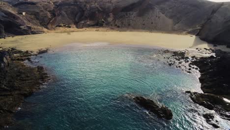 sandy beach near rocky terrain and blue ocean water in lanzarote island, aerial view