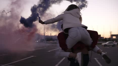 Close-Up-Footage-Of-Two-Crazy-Young-Couples-Whirling-With-Colorful-Smoke-Bombs-In-Hands-On-The-Empty-Parking-Zone-Outside