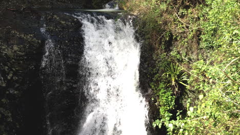 Slo-Mo-tilt-shot-flowing-water-at-Natural-Bridge-Waterfall-Springbrook,-Queensland