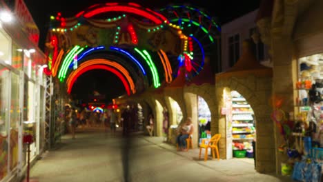 entrance in amusement park at night, people walk and bay souvenirs.