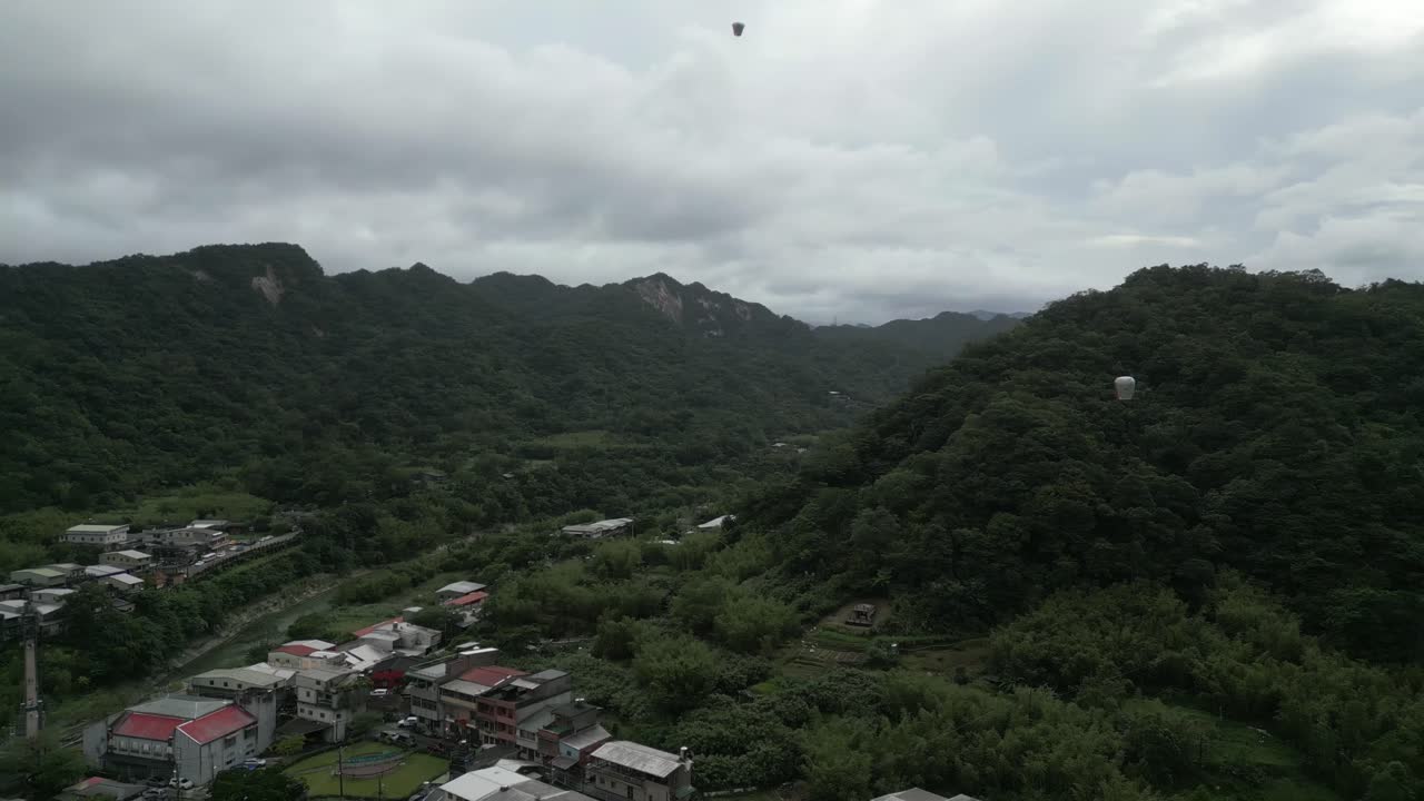 Aerial View of a Village in a Mountain Valley with Hot Air Balloons