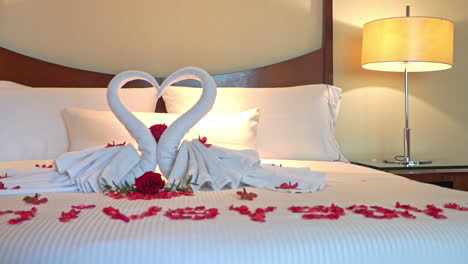 happy anniversary spelled with rose petals on the bed and towels shaped like swans form a heart