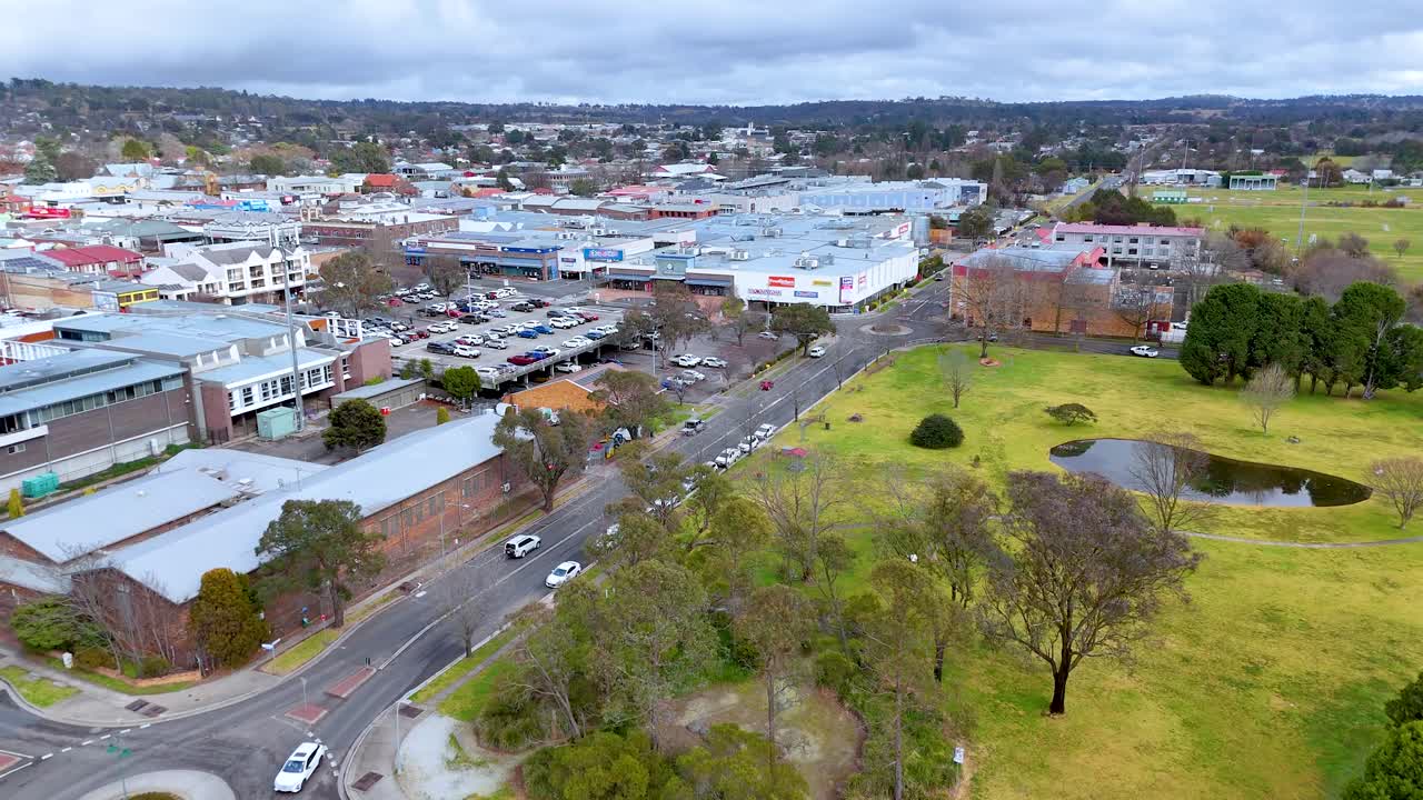 Drone footage glides above a suburban road, roundabout, and green parkland in Armidale, Australia, under overcast daylight with steady, smooth camera movement