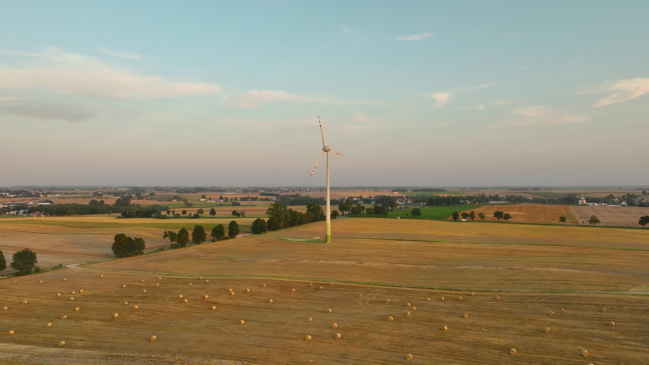 Single wind turbine standing tall in rural farmland, aerial landscape with agricultural fields and village in distance